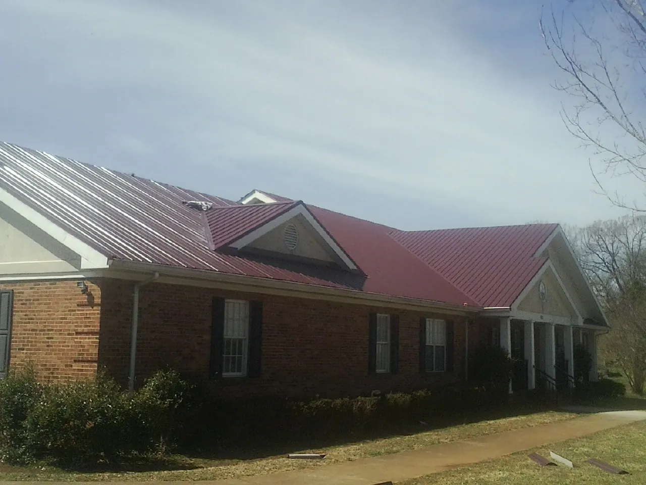 Red metal roof with gabled entries on a long brick building, from a Hail Damage Roof Repair job in Indiantown