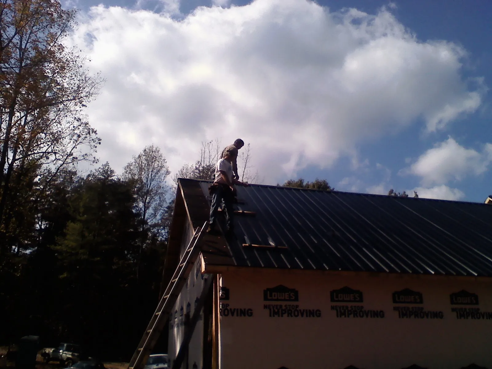 Roofer fastening dark metal panels high against a cloudy sky, from a Roof Inspection job in Indiantown